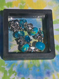 Bracelet with blue and silver charms in a black display case on a colorful fabric background
