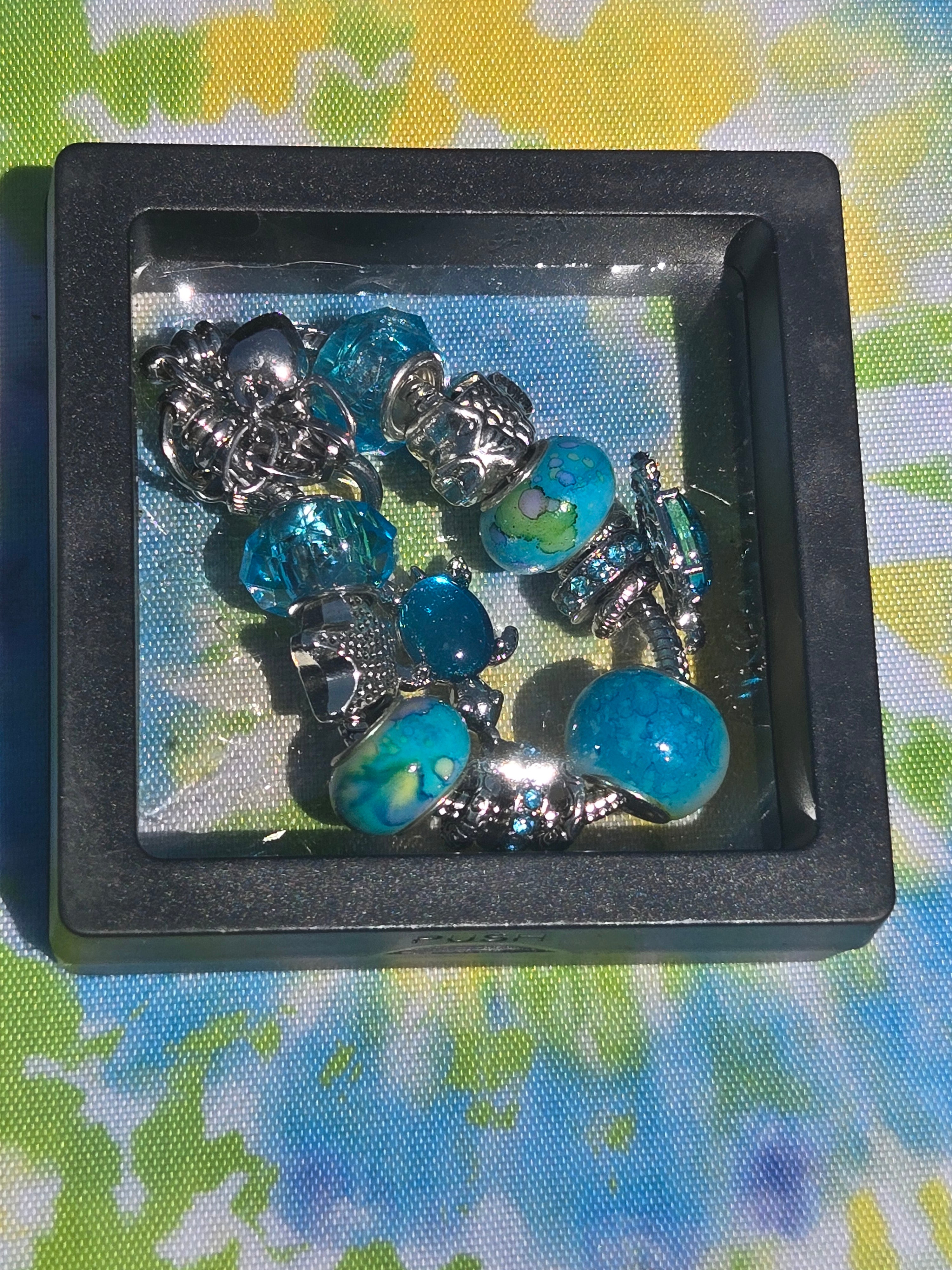 Bracelet with blue and silver charms in a black display case on a colorful fabric background